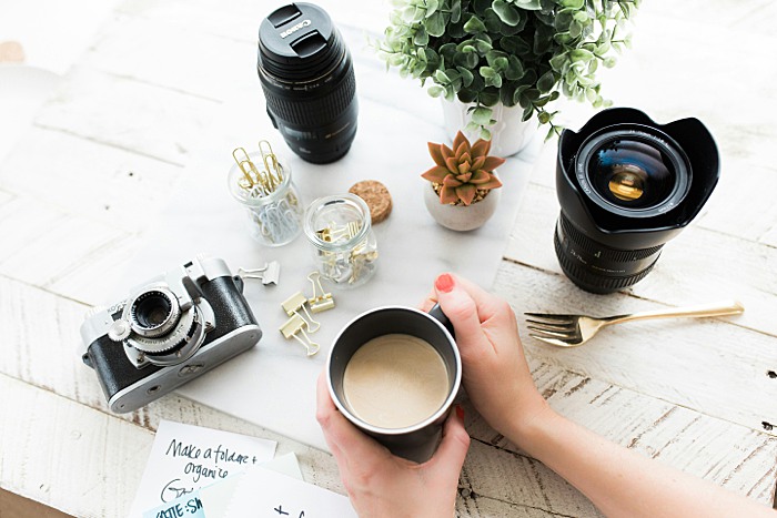 Photographer having coffee with lenses and camera gear around her. Make more time in your photography business with these three simple steps.